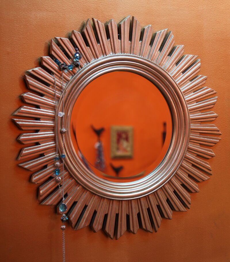 Miroir soleil argenté sur un mur orange